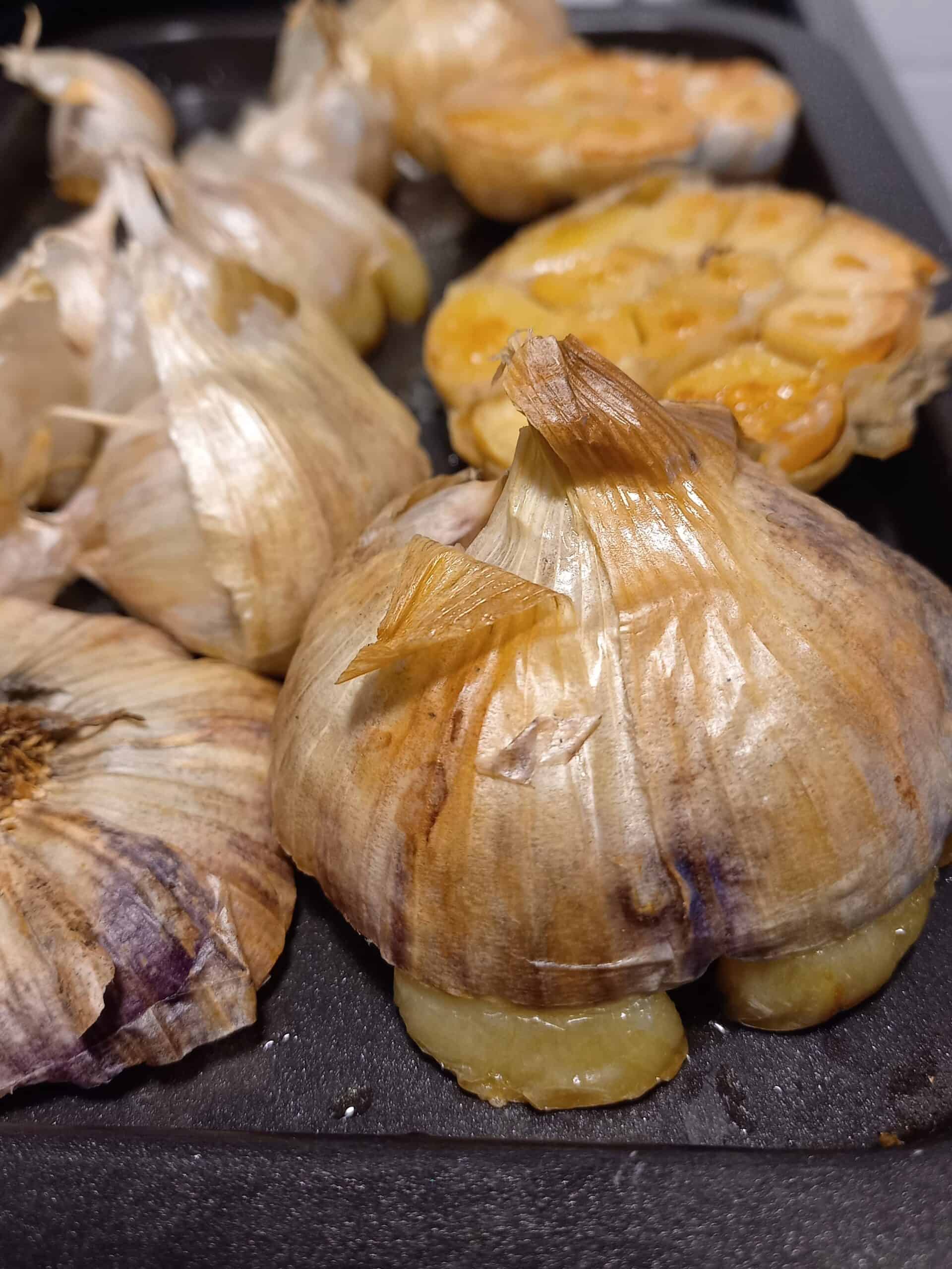 roasted garlic heads, skin on and cut in half, on a black baking tray