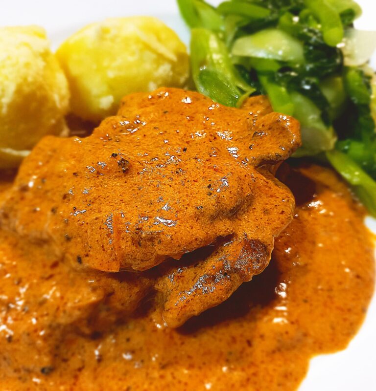 pork pepper steak, in a tomato cream sauce with boiled potatoes and steamed vegetables on a white plate