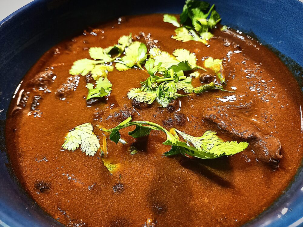 Black bean venison chili in a blue bowl with coriander leaves on top