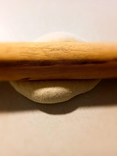 rolling pin on top of pizza dough on a bench top