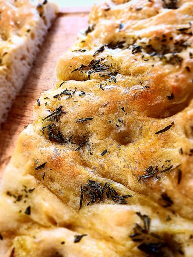 Focaccia bread with rosemary on top cut in half on a wooden chopping board.