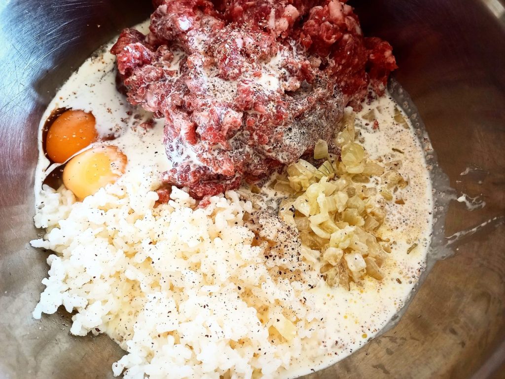 Venison mince, cooked onions, boiled rice, two raw eggs, cream and cracked pepper in a stainless steel bowl