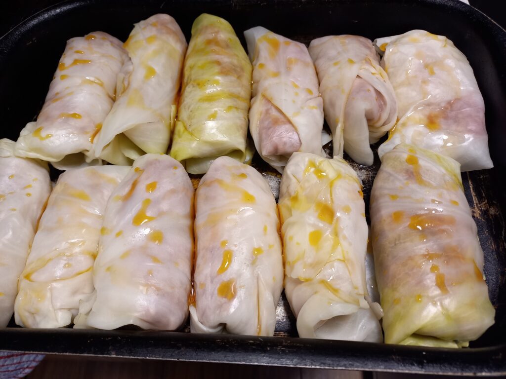12 raw cigar shaped cabbage rolls in a black baking dish drizzled with golden syrup
