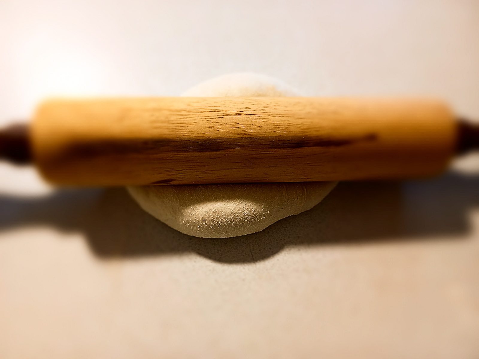 rolling pin on top of pizza dough on a cream colored bench top