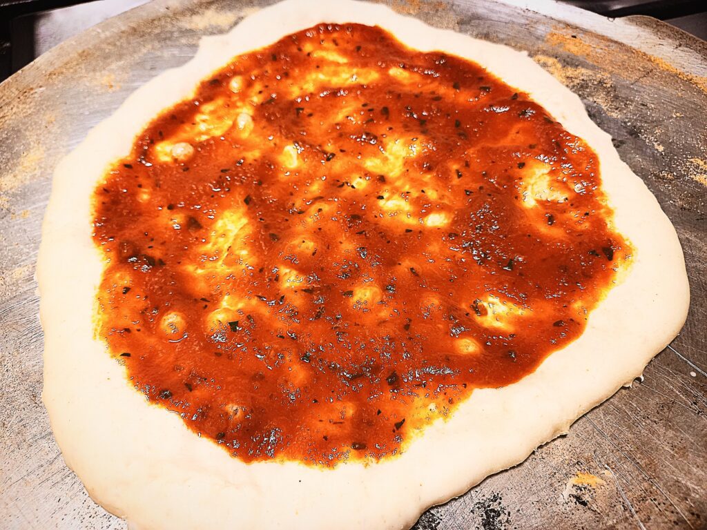 Uncooked pizza base with sauce on top. Sitting on an aluminum pizza tray