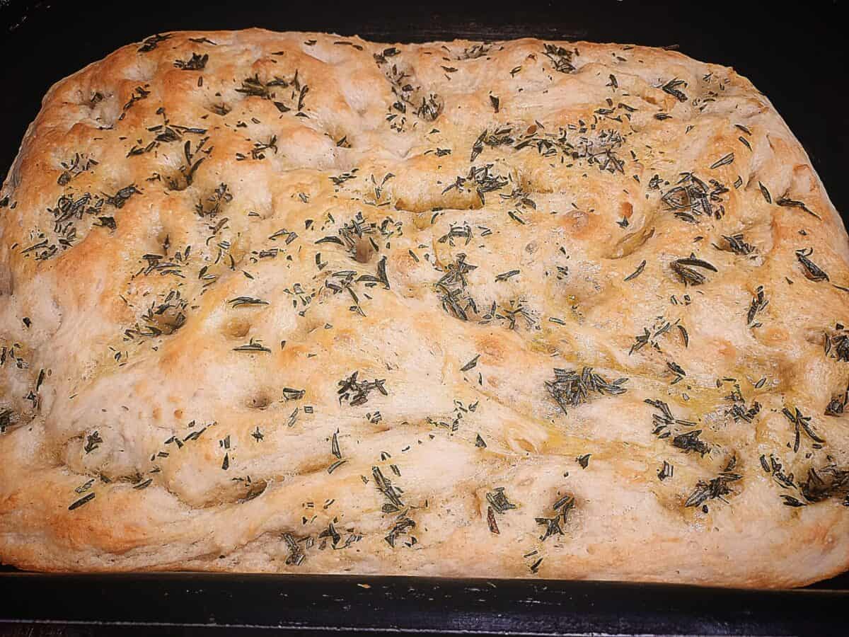 Focaccia bread topped with rosemary in a baking tray.