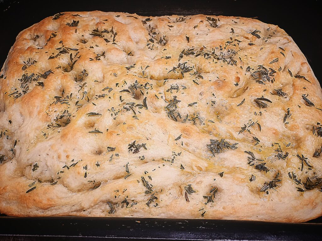 Focaccia bread topped with rosemary in a baking tray.