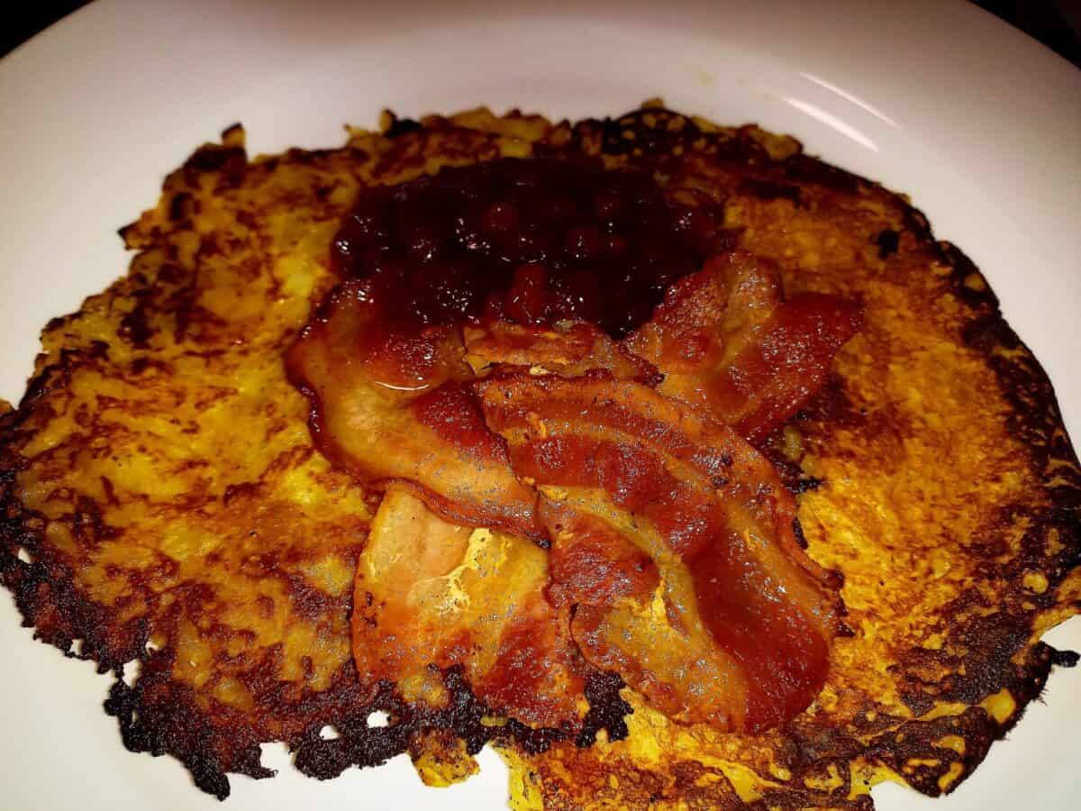 Raggmunkar topped with crispy bacon and lingon berry jam on a white plate