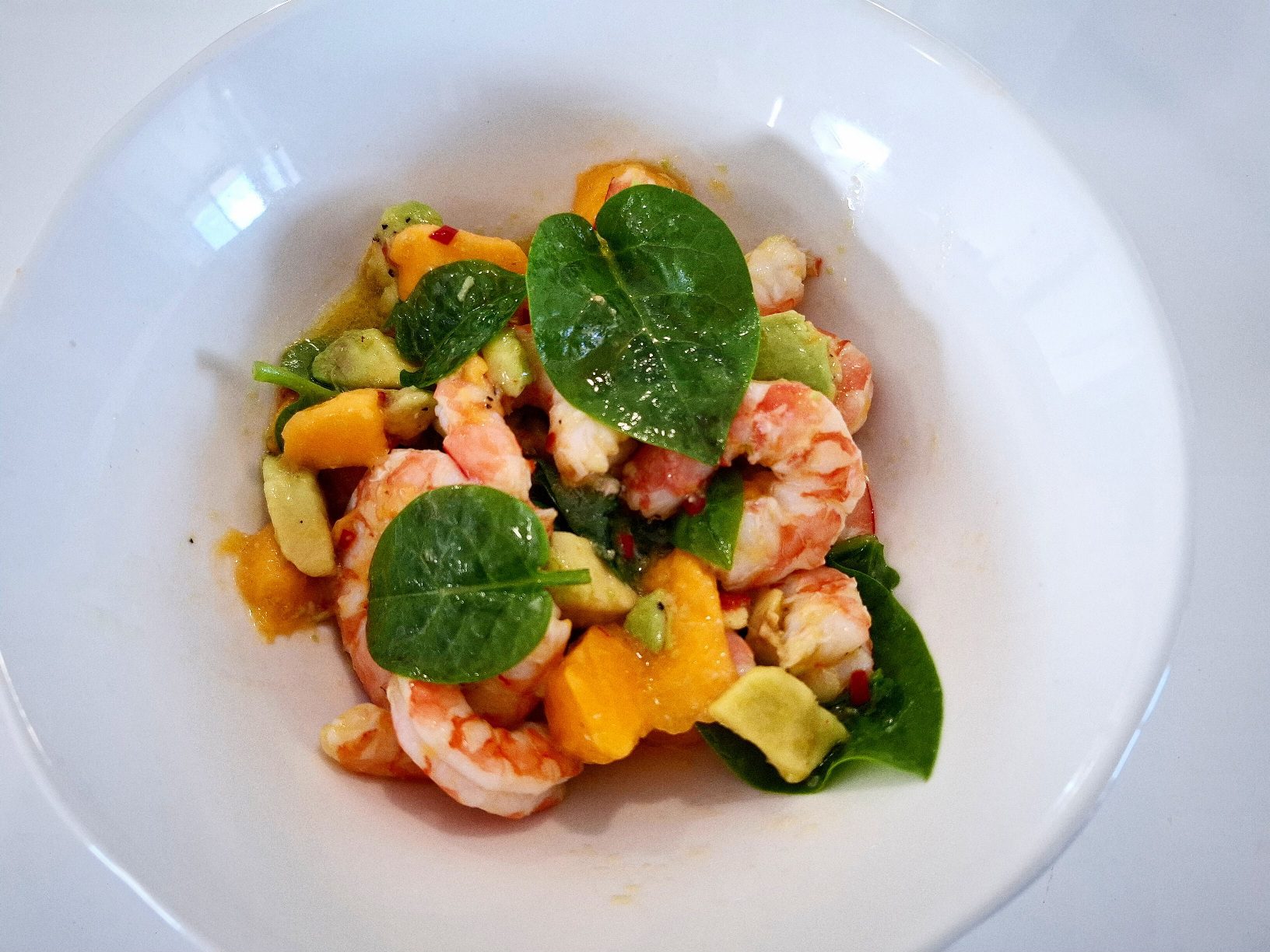 Salad prawn, baby spinach, mango and avocado in a white bowl plate on a white table