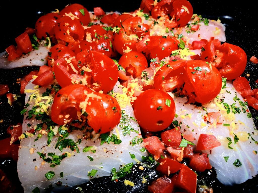 4 Fish fillets in an oven tray topped with cherry tomatoes, diced tomatoes, parsley, lemon zest and chopped garlic