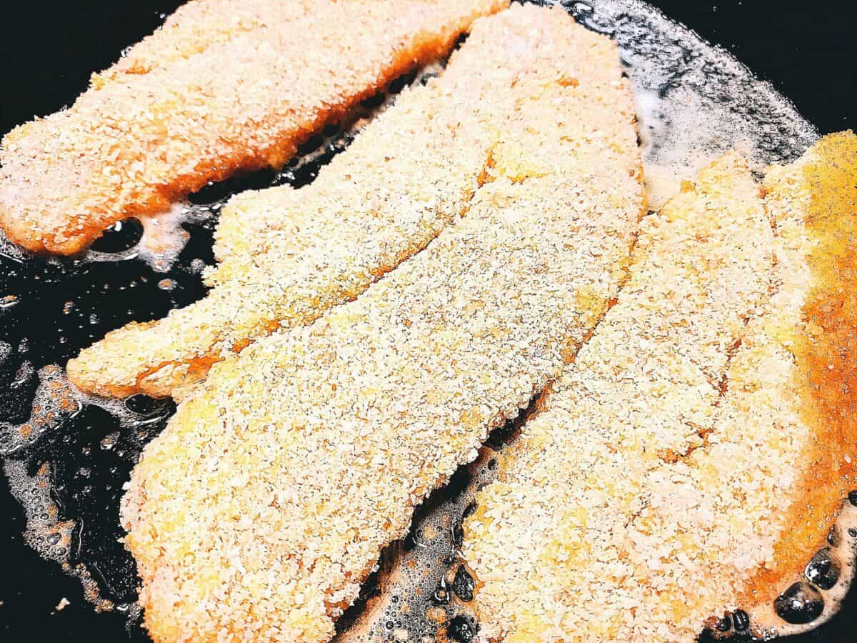 Three crumbed fish fillets frying in a cast iron skillet pan