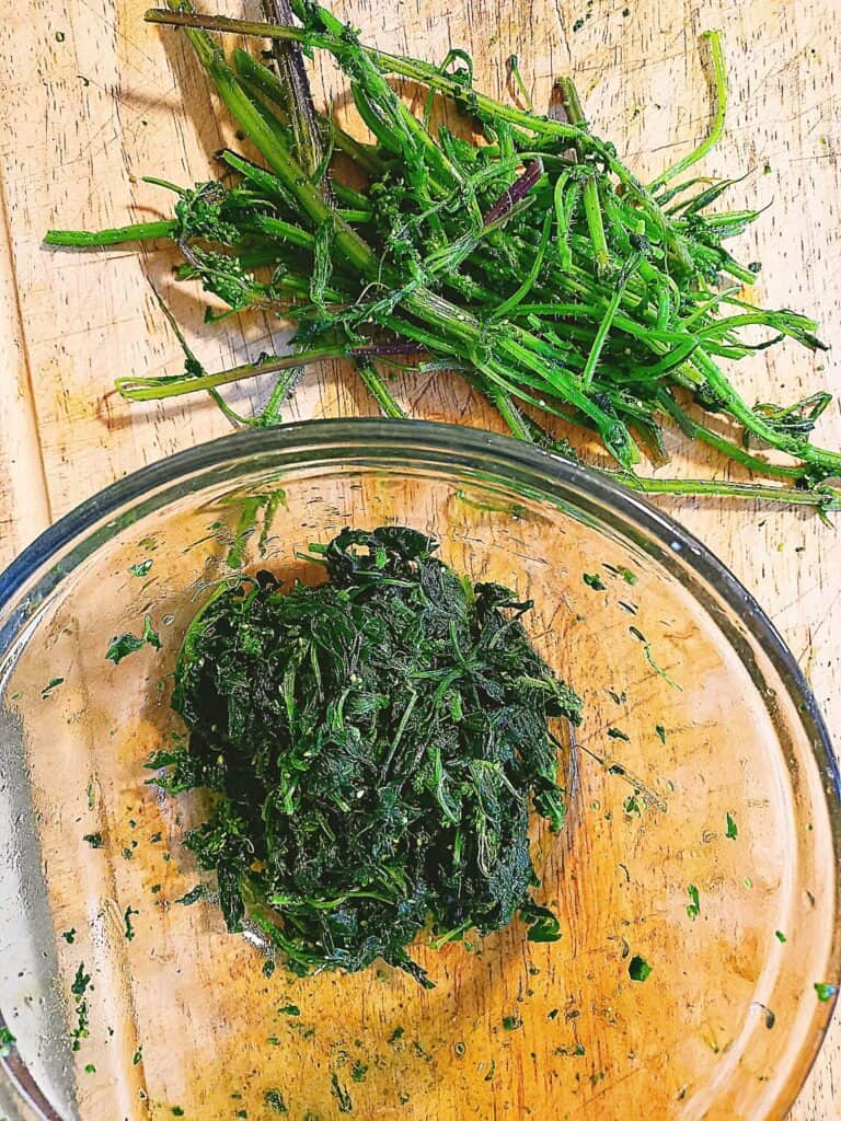 cooked stinging nettles. Leaves picked from the stalks. Cooked leaves in a glass bowl and stalks on a chopping board