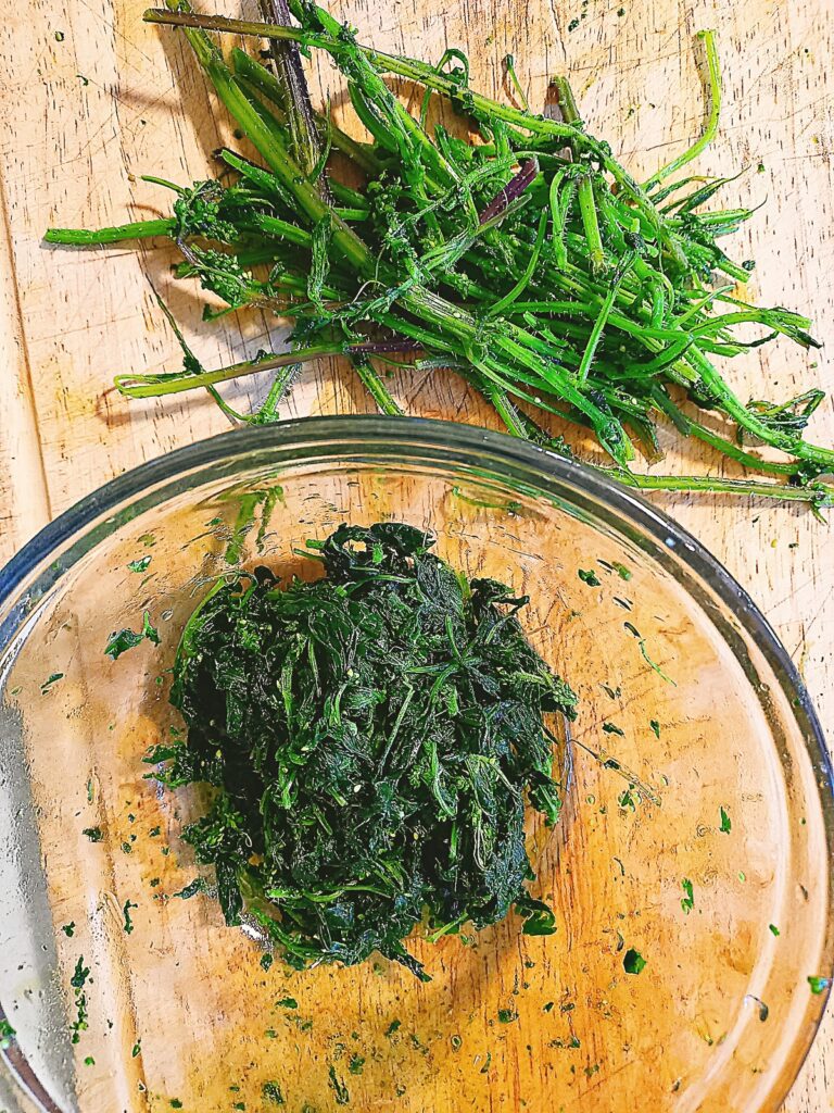 cooked stinging nettles. Leaves picked from the stalks. Cooked leaves in a glass bowl and stalks on a chopping board