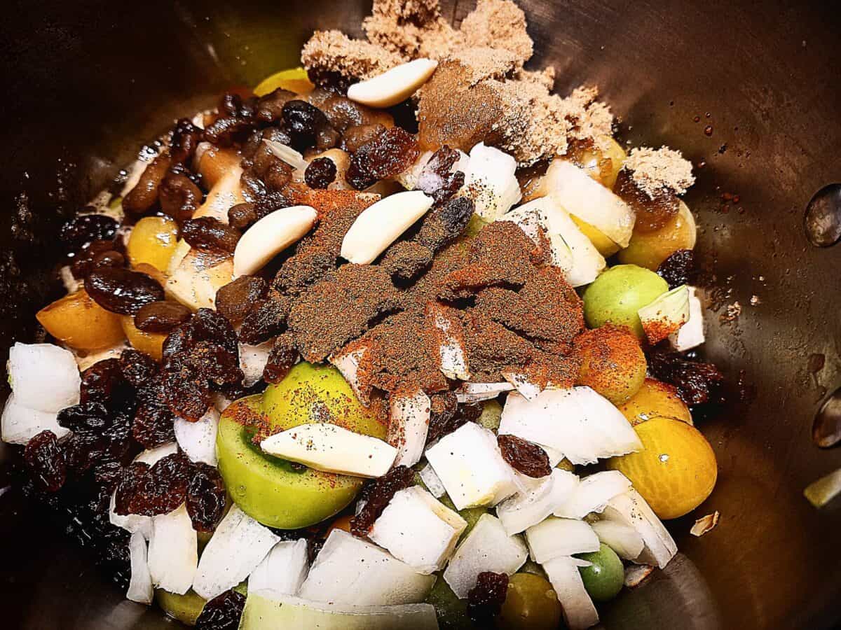 A close up of all the raw ingredients for green tomato and chili chutney in a deep sauce pan
