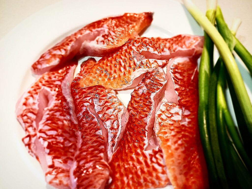 6 raw scarlet wrasse fillets on a plate with a bunch of spring onions