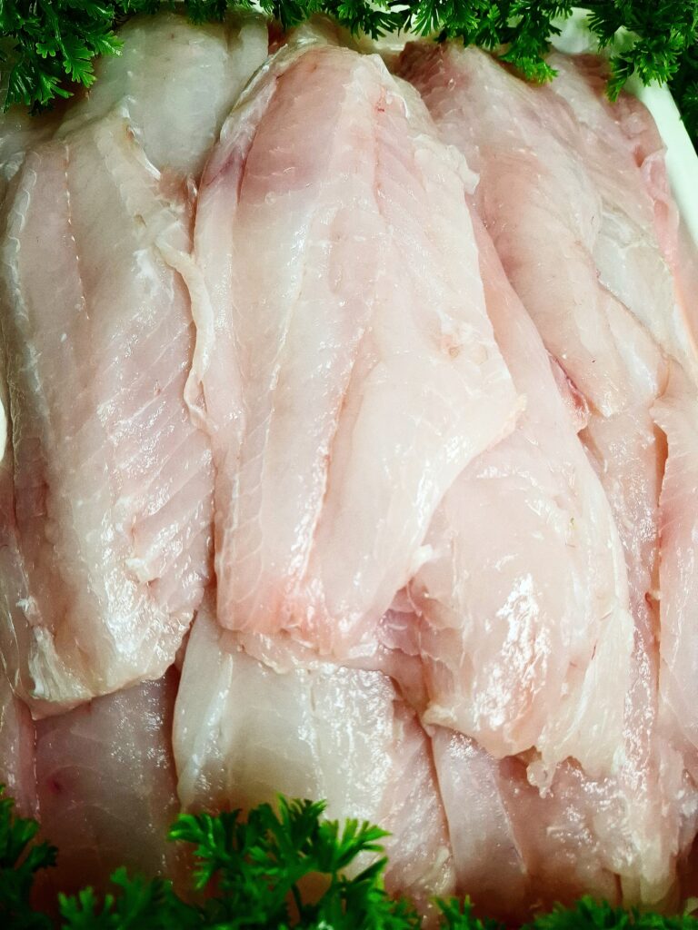 A lot of fresh fish fillets laid out on o white tray decorated with fake parsley at the top and bottom