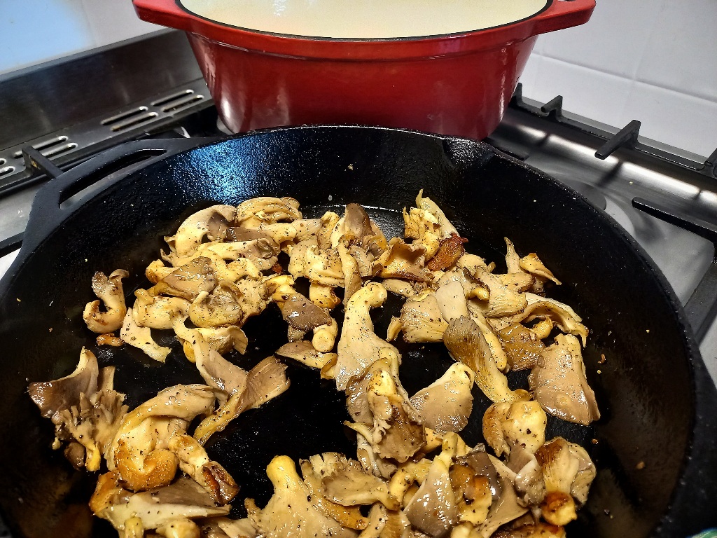 Frying mushrooms until golden in a skillet pan. A red dutch oven in the background