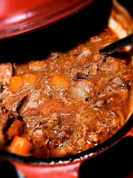 venison stew in a red dutch oven with a ladle in it