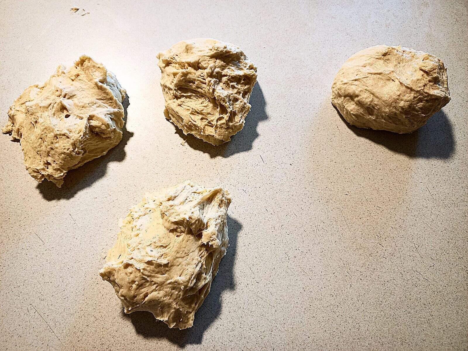 4 round pizza dough balls on a cream colored work bench