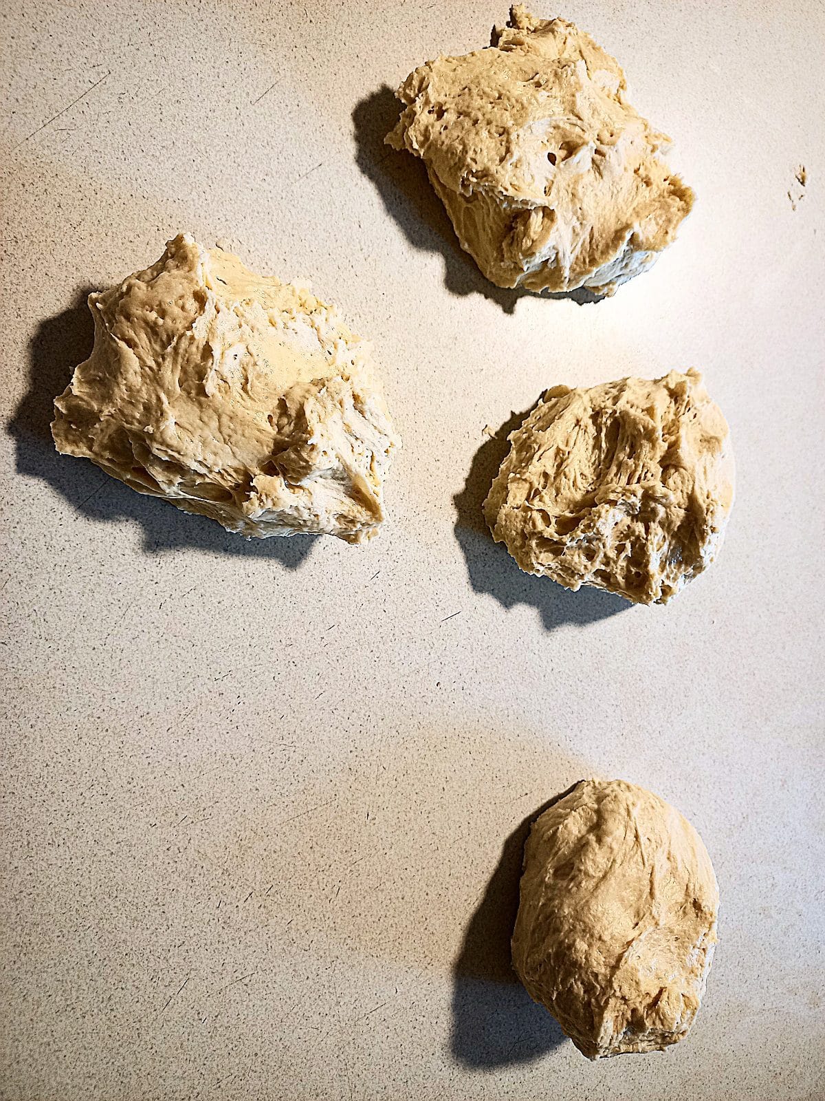 4 round pizza dough balls on a cream colored work bench