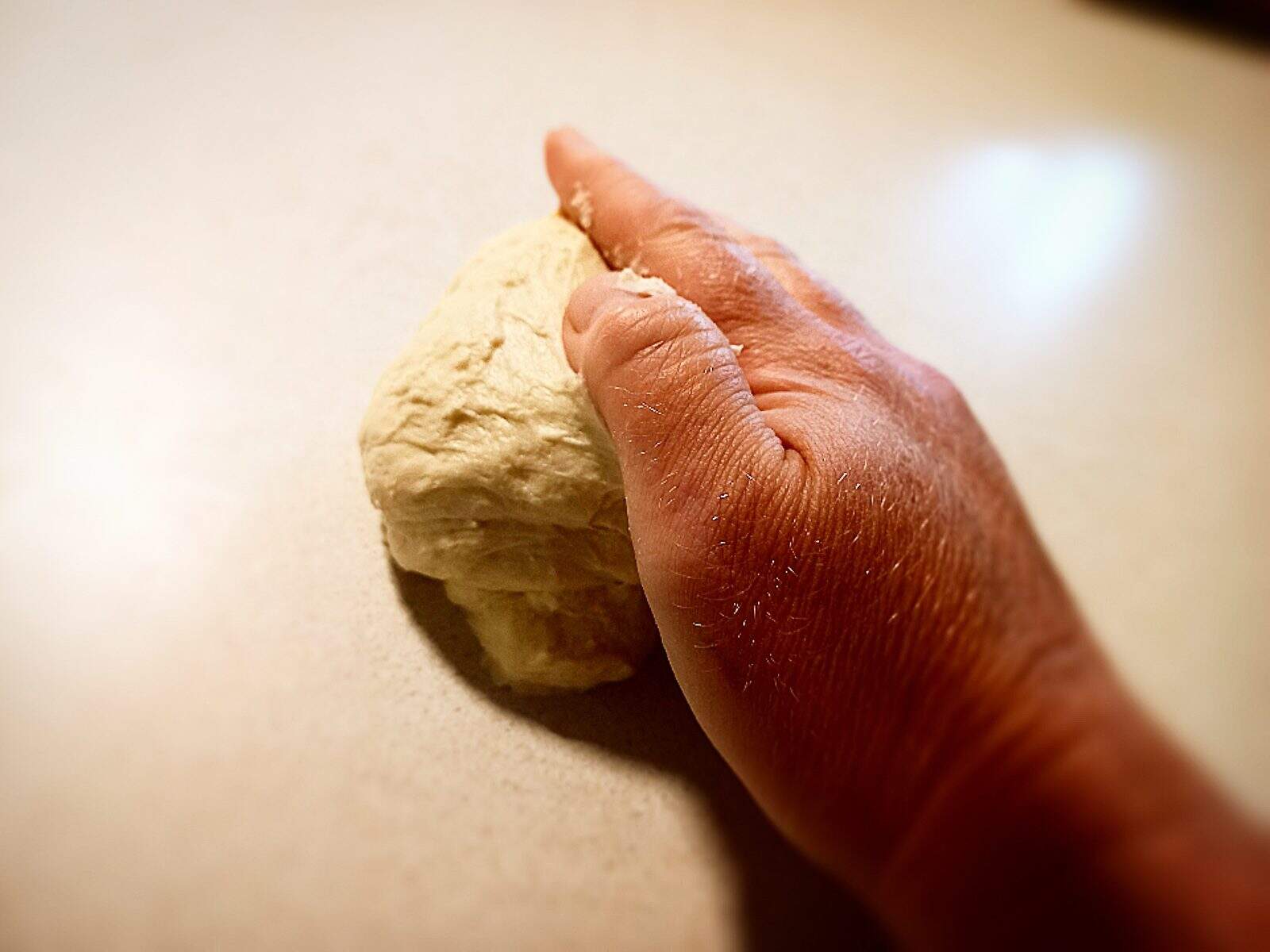 rolling the pizza dough with the palm of my hand on a cream colored work bench