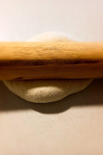 rolling pin on top of pizza dough on a cream colored bench top