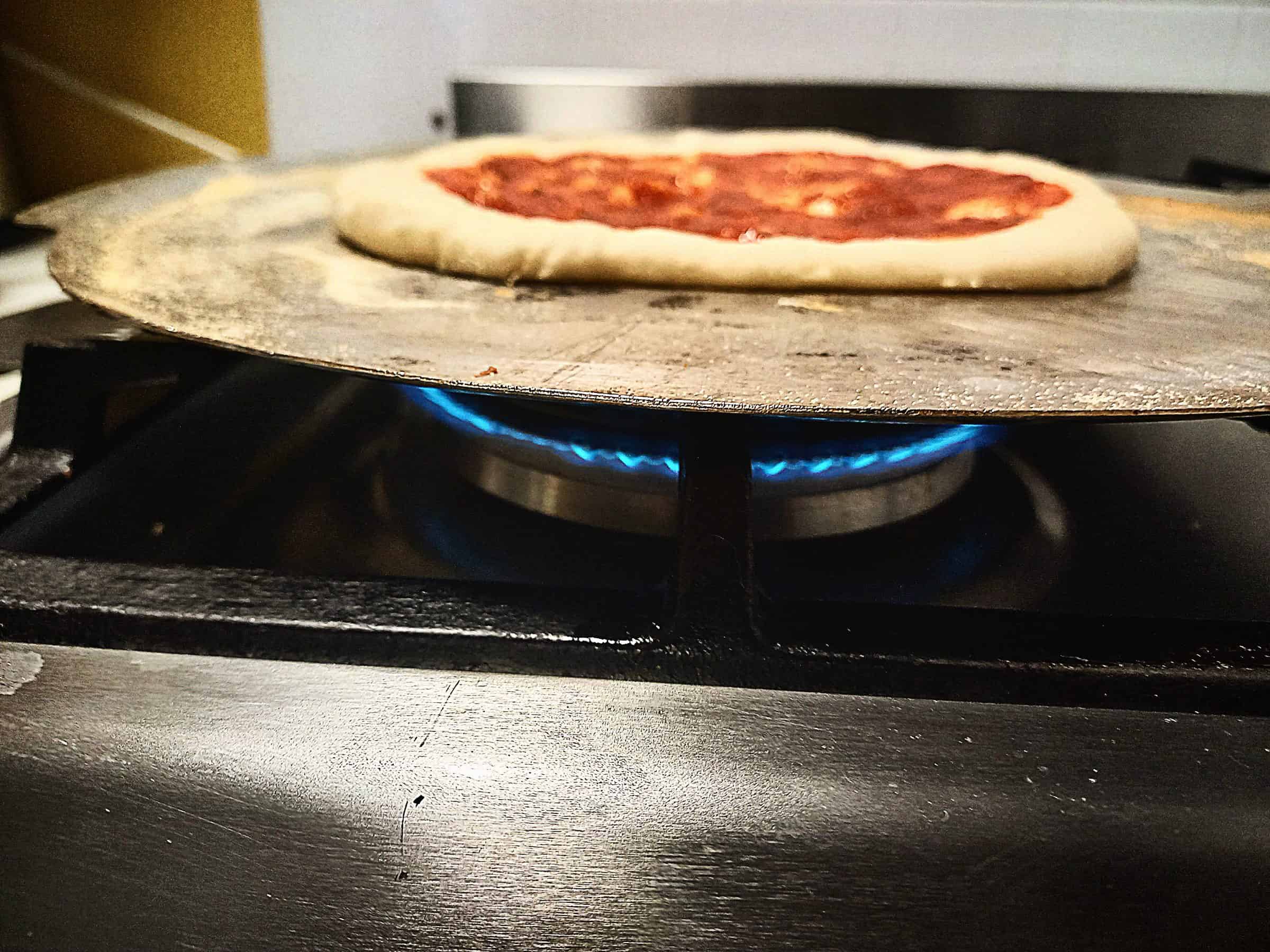 Raw pizza base topped with pizza sauce cooking on a gas burner.