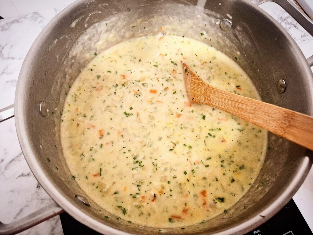 Fresh herbs added to the crab meat and vegetable chowder. In a large saucepan with a wooden spoon on a marbled bench top.