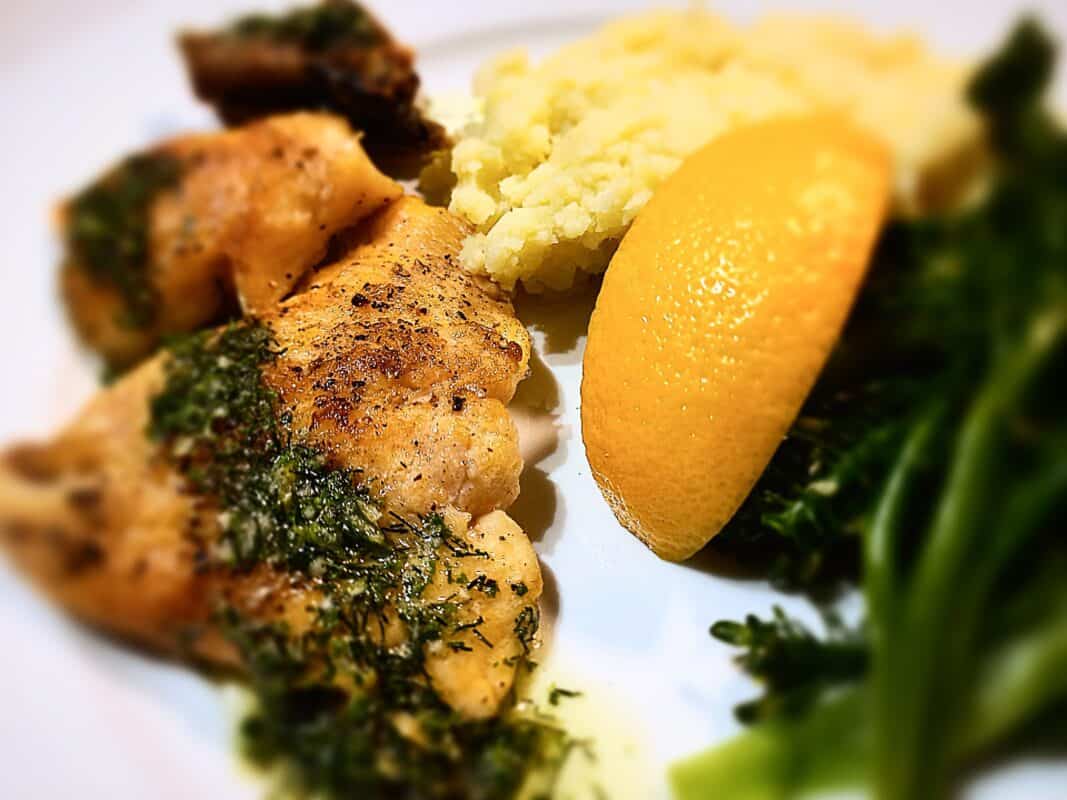 trout crispy skin with mash potatoes, lemon wedge and broccolini on a white plate