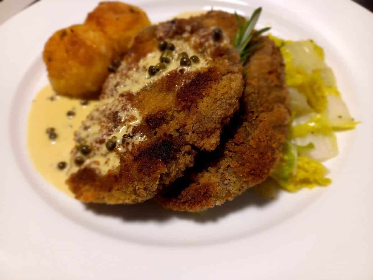 Schnitzel with green peppercorn sauce, potatoes and cabbage on a white plate