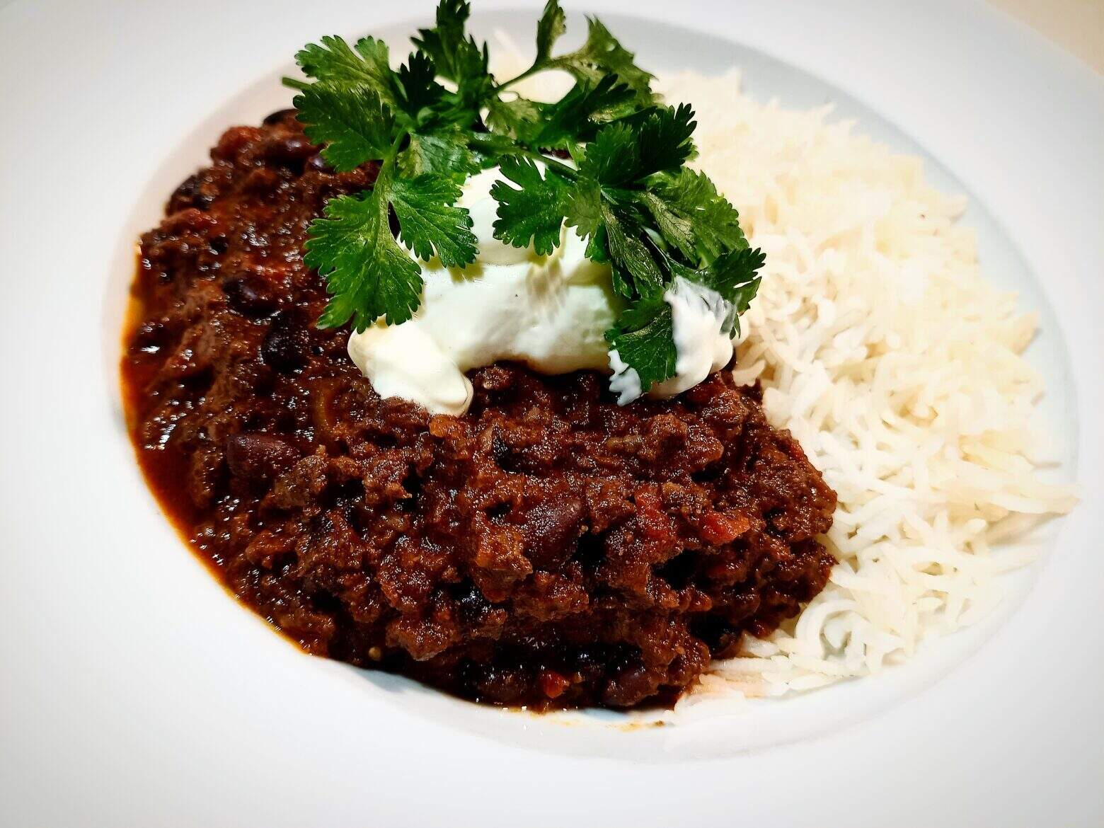 Venison chili with rice topped with sour cream and fresh coriander leaves.