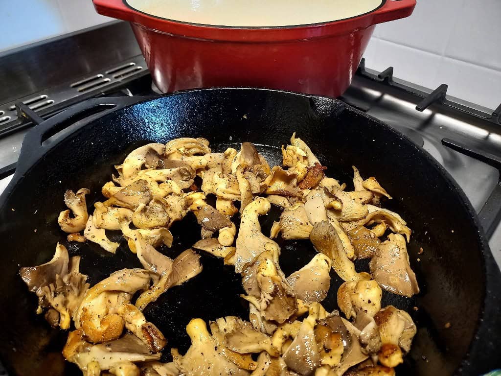 Frying mushrooms until golden in a skillet pan. A red dutch oven in the background