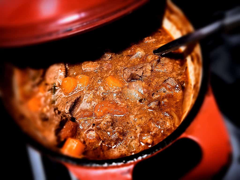 venison stew in a red dutch oven with a ladle in it