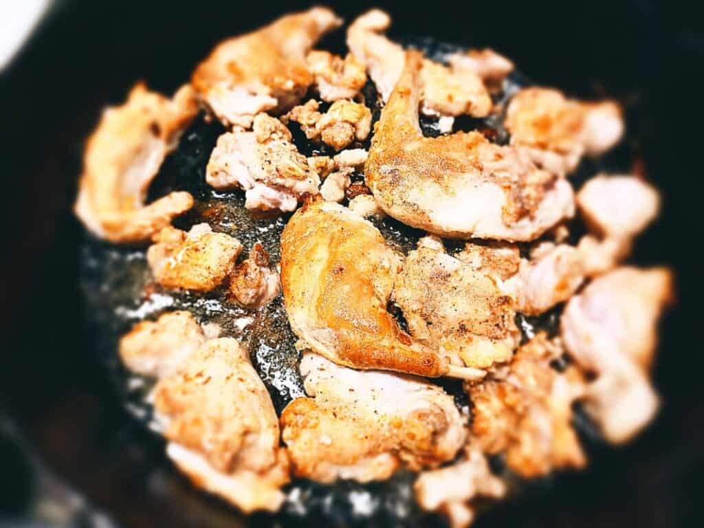 Rabbit pieces frying in a cast iron skillet pan until golden brown
