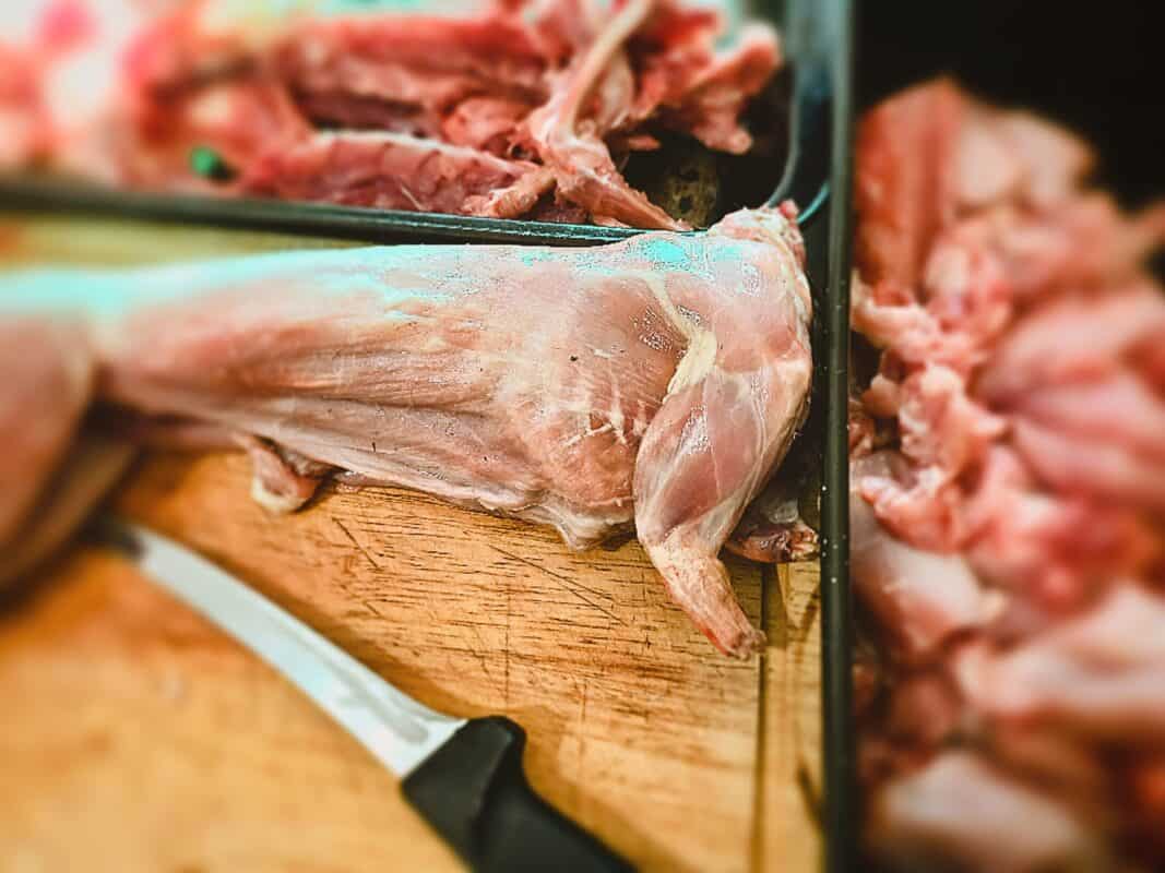 Skinned rabbit and a knife on a chopping board. Rabbit meat in two trays next to the chopping board