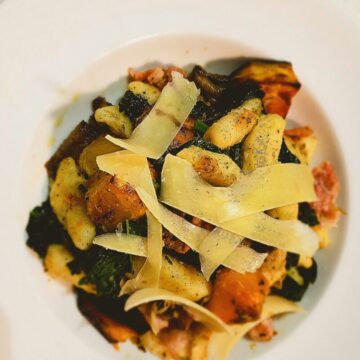 Roasted vegetable gnocchi in a white bowl plate parmesan cheese shavings on top