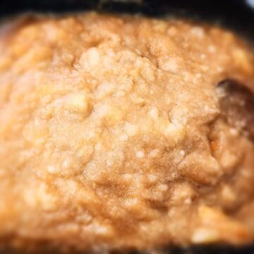 Applesauce compote cooking in a large square sauce pan. A wooden spoon stirring the sauce