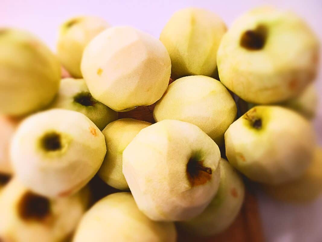Many peeled apples on a white bench top