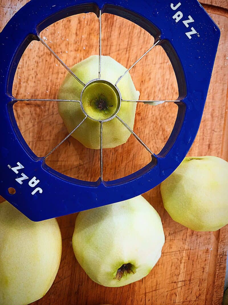 peeled apples on a wooden chopping board. An apple slicer ready to cut the apples