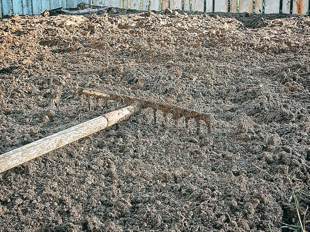 Hard tooth rake laying on top of the garden bed. A wooden fence in the back ground