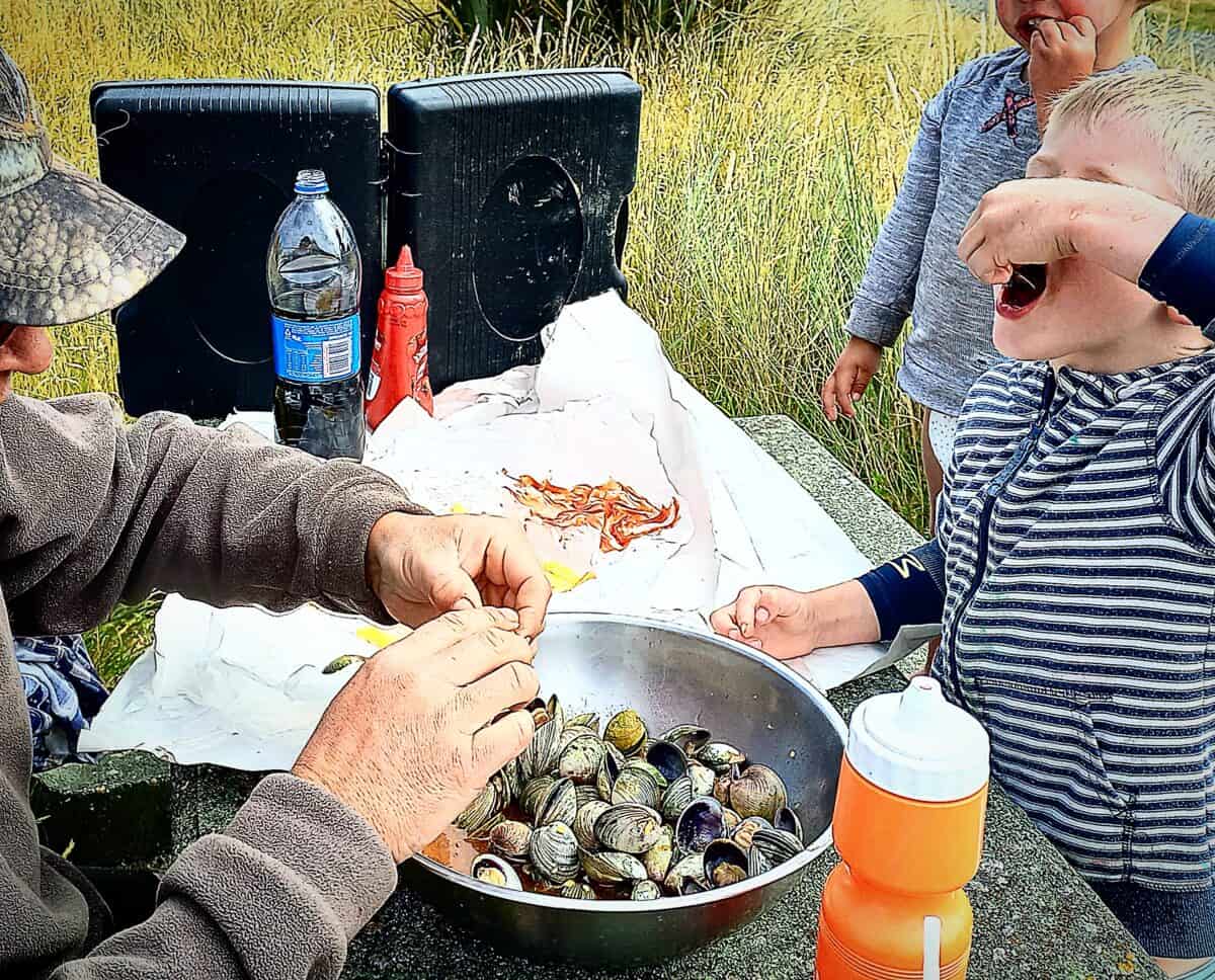 A dad and two children eating fresh clams on a picnic table