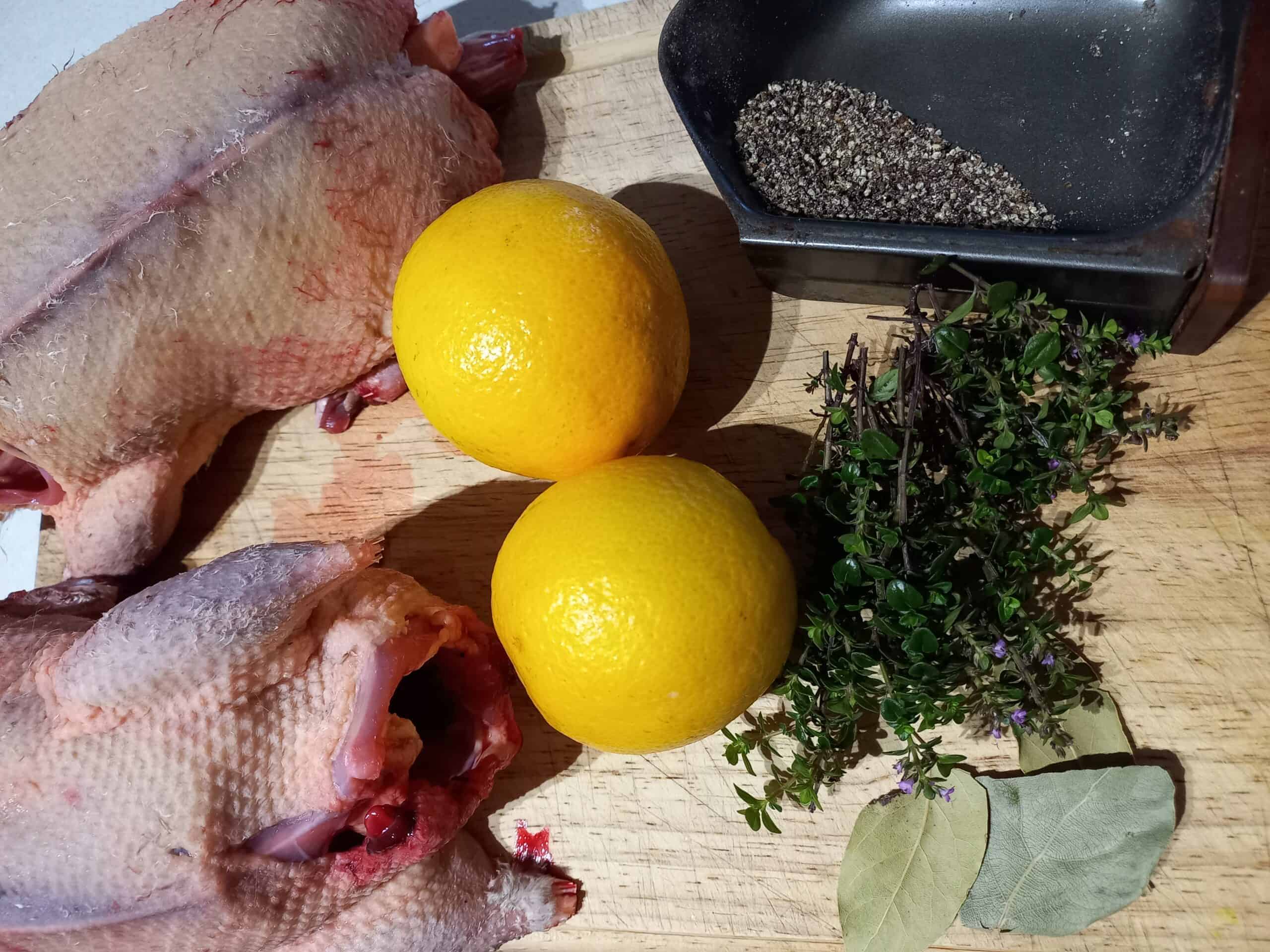 Two raw wild ducks on a chopping board with 2 oranges, fresh thyme, three bay leaves and cracked black pepper