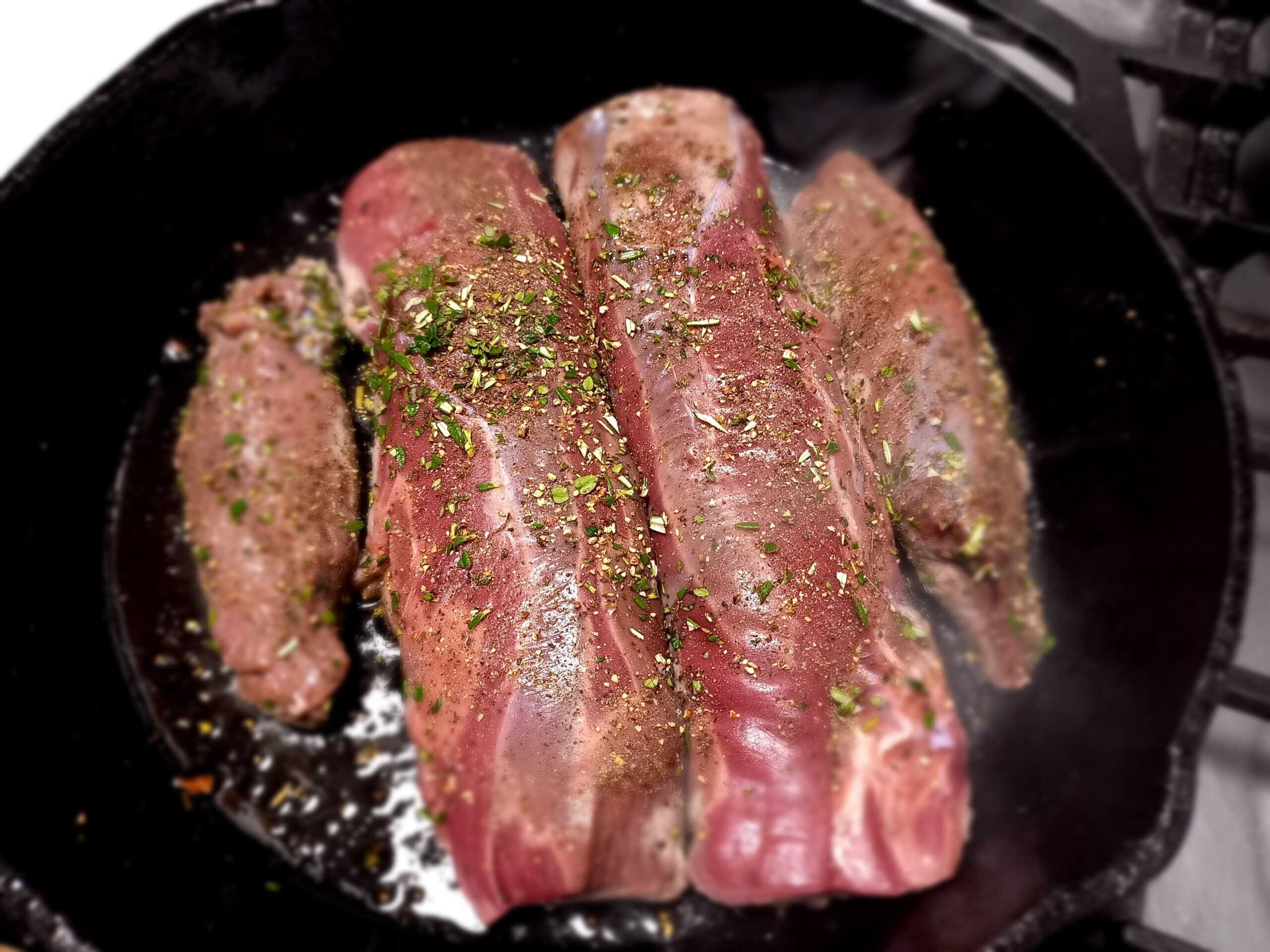 cooking venison meat in a skillet frying pan with chopped herbs on top
