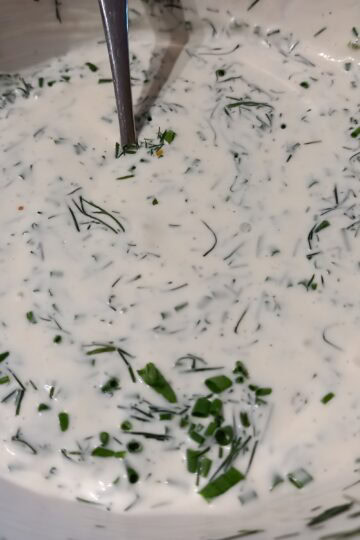 A close up image of sour cream lemon and herb dressing with in a white bowl and a spoon in it