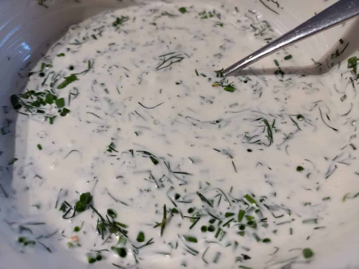 A close up image of lemon herb dressing with sour cream in a white bowl and a spoon in it