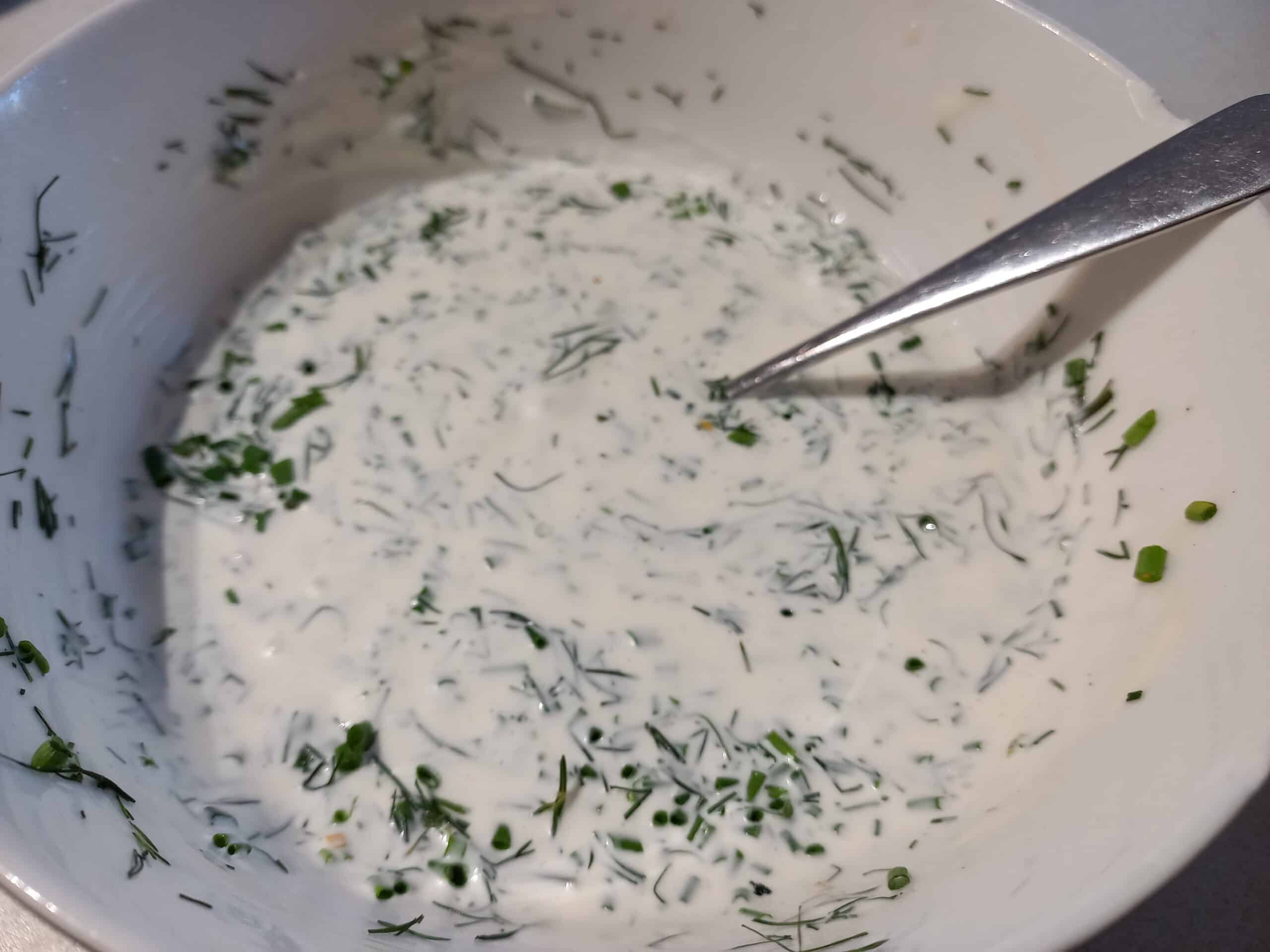Sour cream lemon and herb dressing in a white bowl and a spoon in it