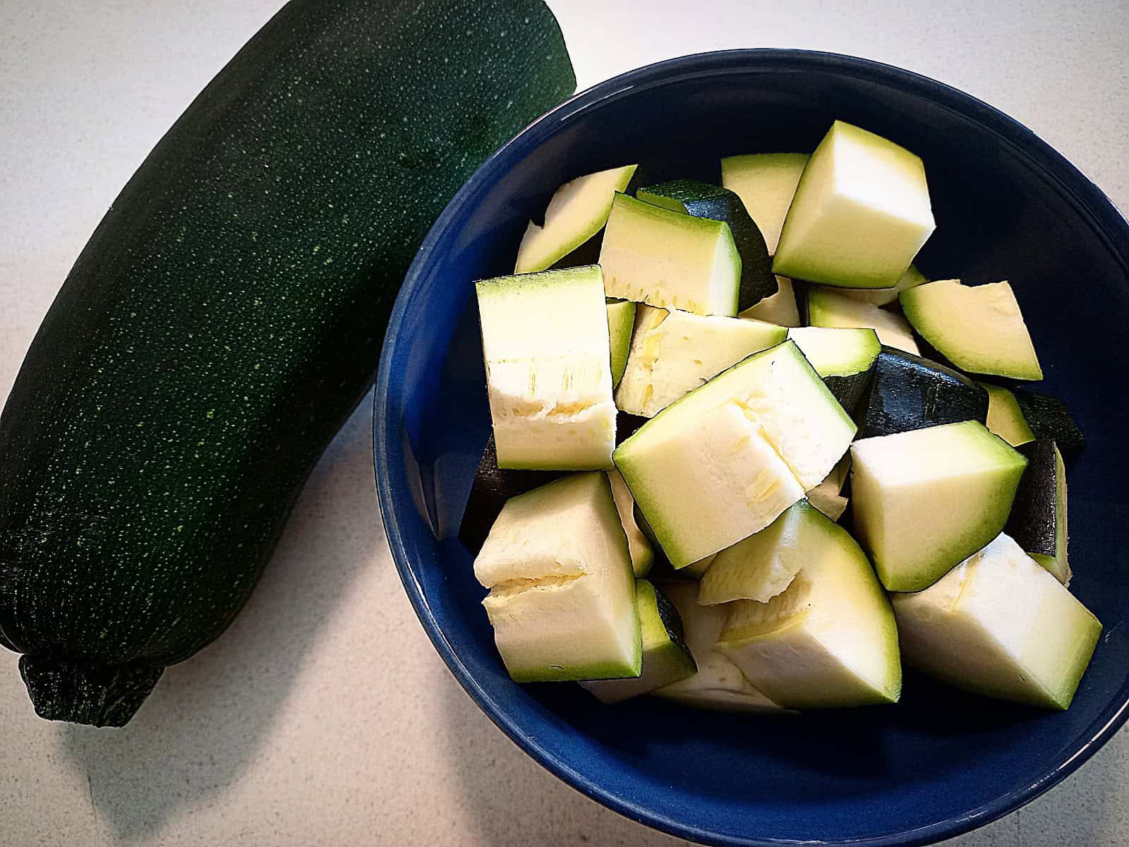 One hole zucchini on a bench and a bowl of large dices of zucchini next to it