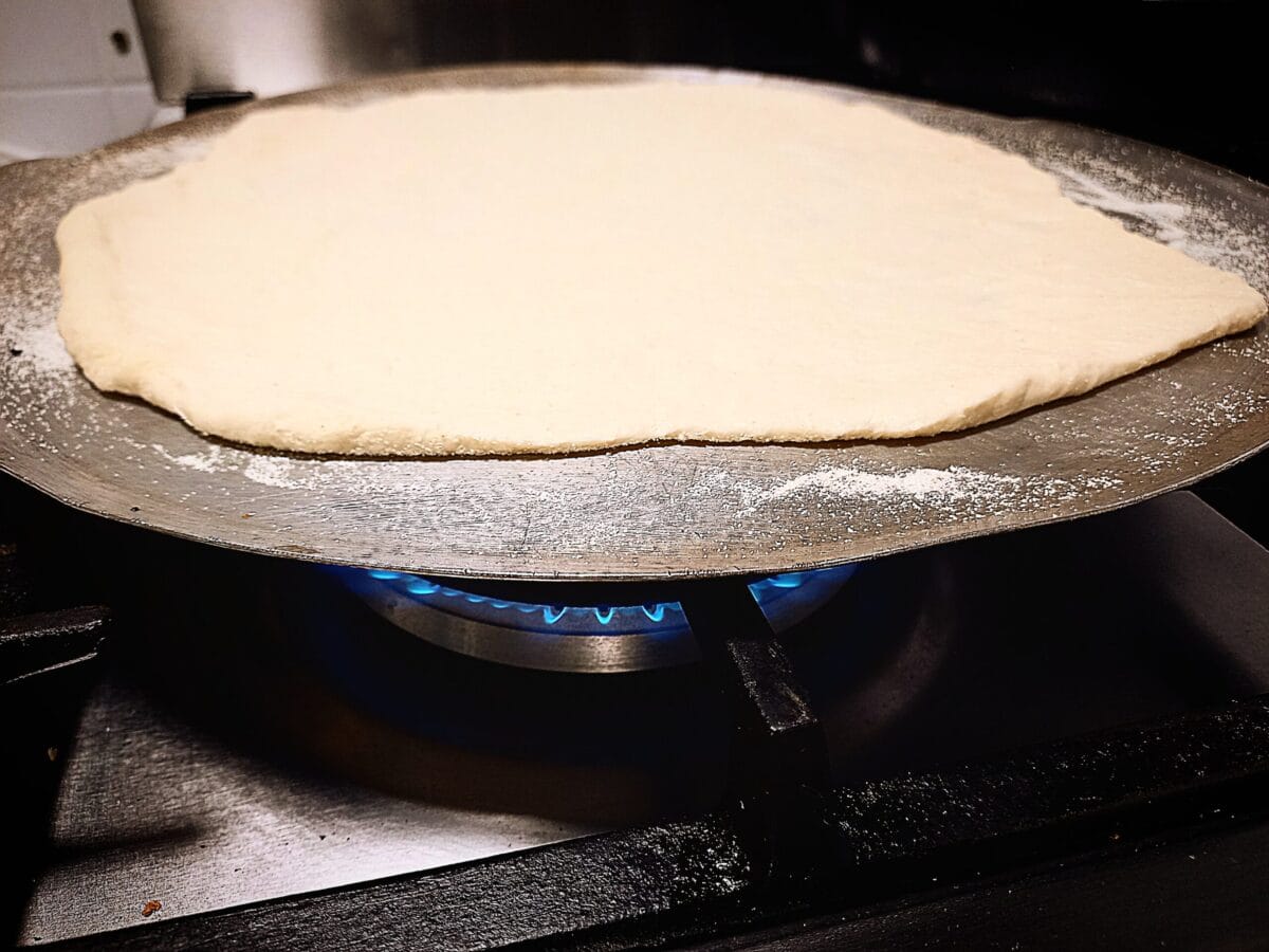 Uncooked Pizza dough on a aluminium tray on top of a gas flame burner