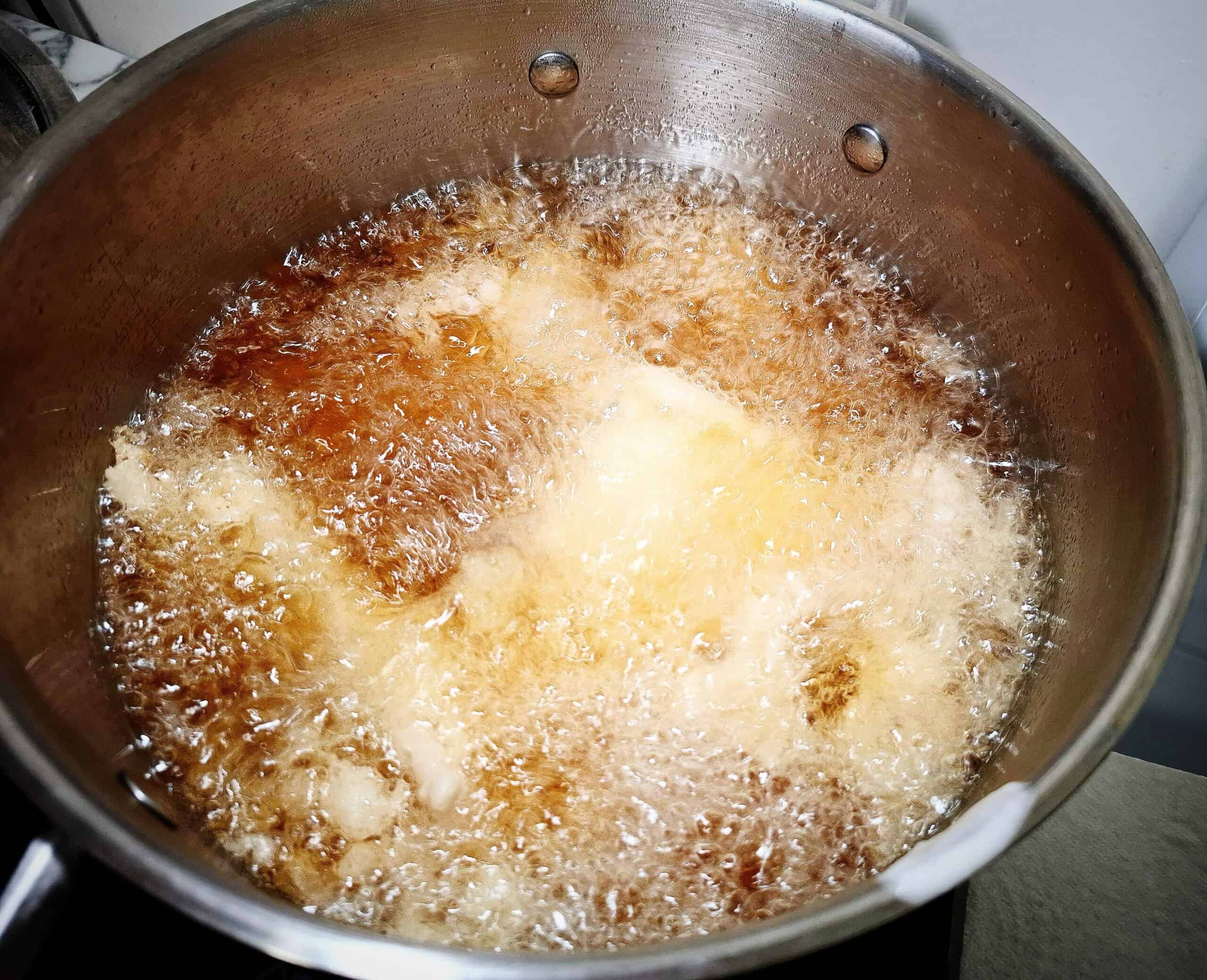 Tempura fish pieces cooking in hot oil in a saucepan.