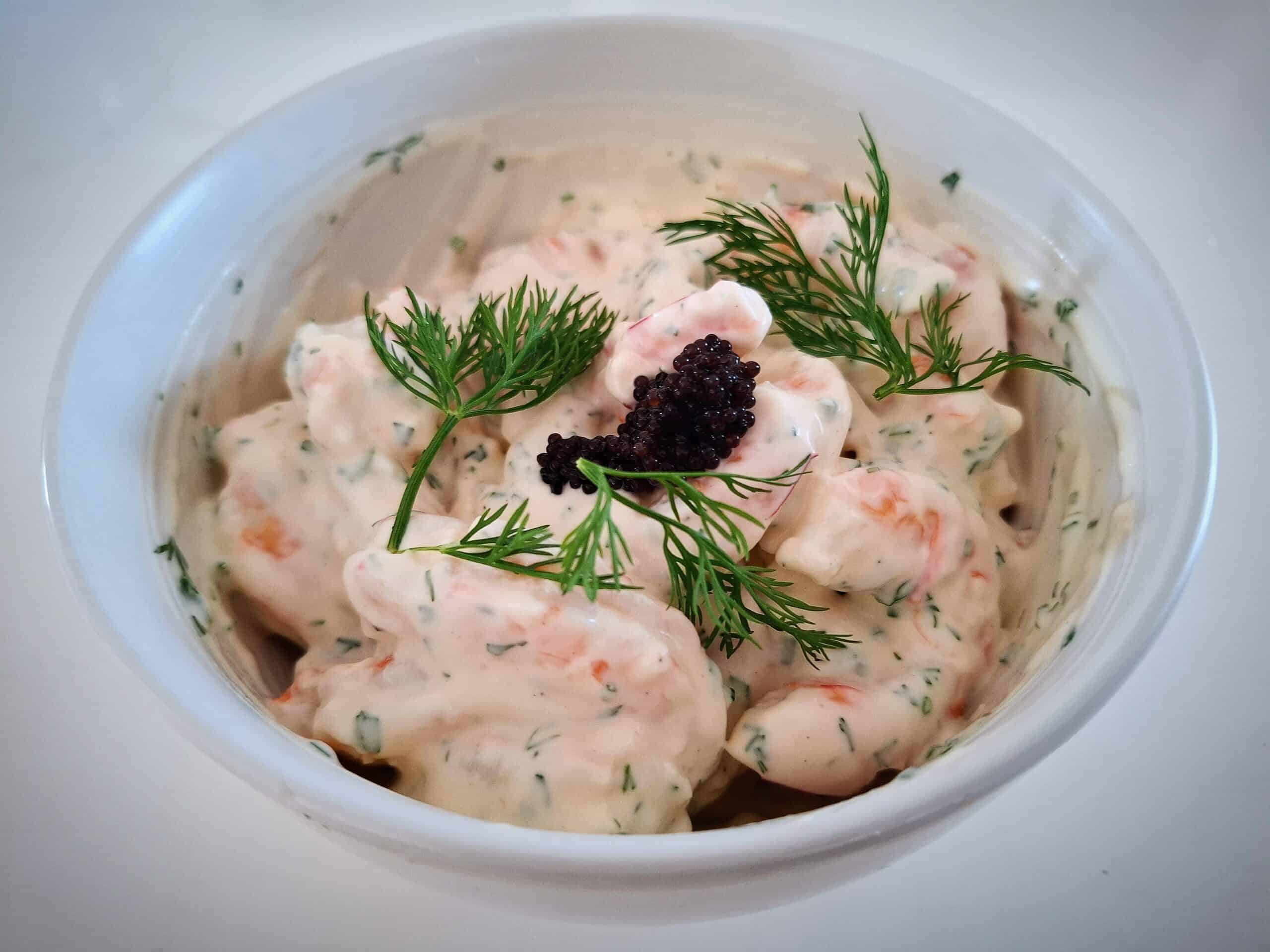 prawn skagen with lump fish caviar and fresh dill on top in a white bowl on a white table